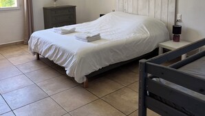 Una cama bien hecha con sábanas y toallas blancas, una mesita de noche con lámpara, una mesita auxiliar y un cuadro en la pared.