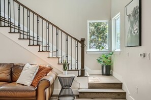 Staircase leads to an upper level with a leather sofa and a view of lush greenery.