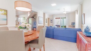 A modern living room with a wooden dining table, a blue sofa, and a red decorative piece. - PF42 Linda Casa 4 Quartos- Villa Firenze (Mata de São João)