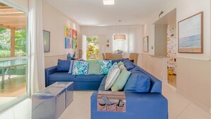 A modern living room with a blue sofa, a glass coffee table, and a ceiling fan. - PF42 Linda Casa 4 Quartos- Villa Firenze (Mata de São João)