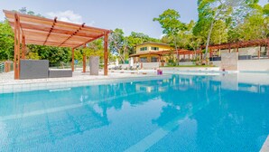 A swimming pool with a wooden pergola, lounge chairs, and a house in the background. - PF42 Linda Casa 4 Quartos- Villa Firenze (Mata de São João)