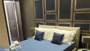 A hotel room with a large bed, a bedside table, a lamp, and a door. - Suite Ursino B&B (Catania)