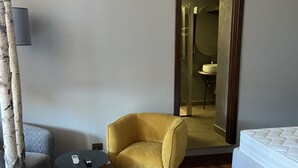 A modern hotel room with a wooden floor, a yellow armchair, a small round table, a sofa, a bed, and a large mirror. - Suite Ursino B&B (Catania)