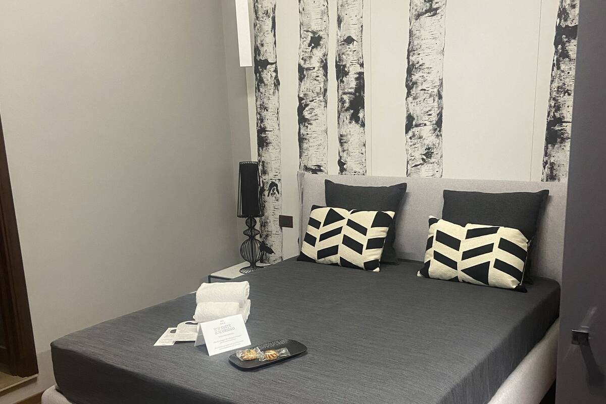 Quarto moderno com uma cama grande, duas almofadas, uma mesinha de cabeceira e uma pequena luminária.