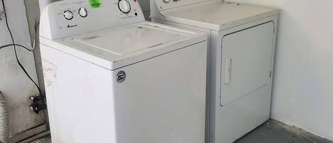 A laundry room with two white front-loading washing machines, a white plastic laundry basket, and visible plumbing.