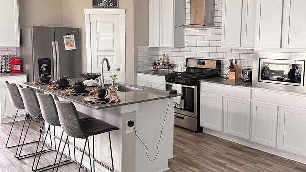 Una cucina moderna con mobili bianchi, un'isola centrale con sgabelli da bar, un frigorifero in acciaio inossidabile e un forno integrato.
