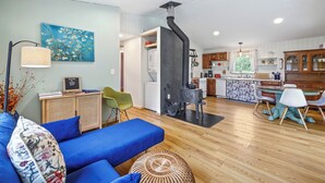 Ein modernes Wohnzimmer mit einem blauen Sofa, einem Essbereich mit Tisch und Stühlen sowie einer Küche mit Holdekor-Schränken und einem schwarzen Herd.