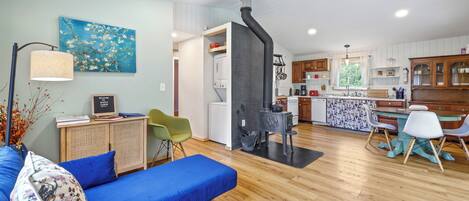 Un salon moderne avec un canapé bleu, un coin repas comprenant une table et des chaises, et une cuisine dotée de meubles en bois et d’une cuisinière noire.