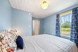 Ein Schlafzimmer mit einem Bett, einem Nachttisch, einem Fenster mit Vorhängen und einer Deckenleuchte.