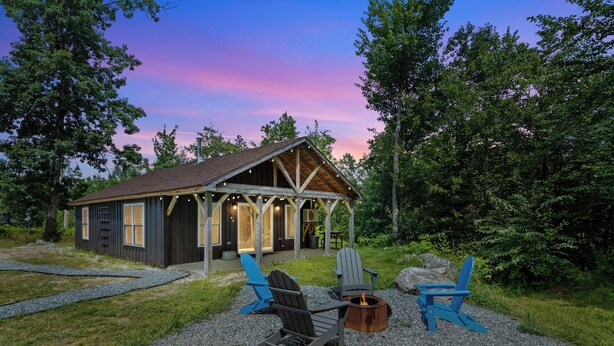 Eine Hütte mit Veranda, zwei Adirondack-Stühlen und einem Feuerkorb.