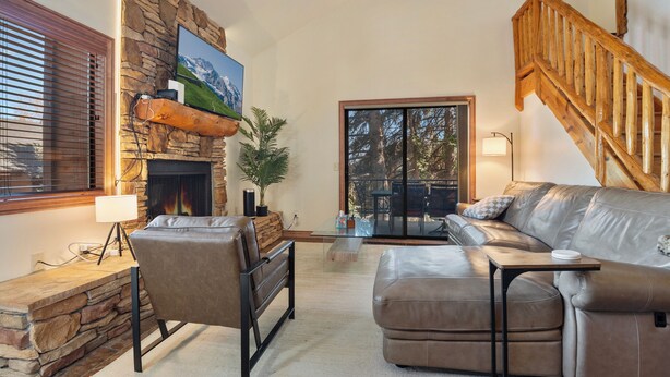 A living room with a stone fireplace, leather sofa, and a wooden staircase. - Red Pine Condos by Park City Vacations (Park City)