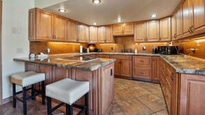 A kitchen with wooden cabinets, granite countertops, and a central island with stools. - Red Pine Condos by Park City Vacations (Park City)