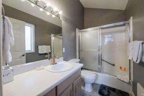 Features a large vanity with dual sink and mirror, separate shower area with glass door, and a bathtub.