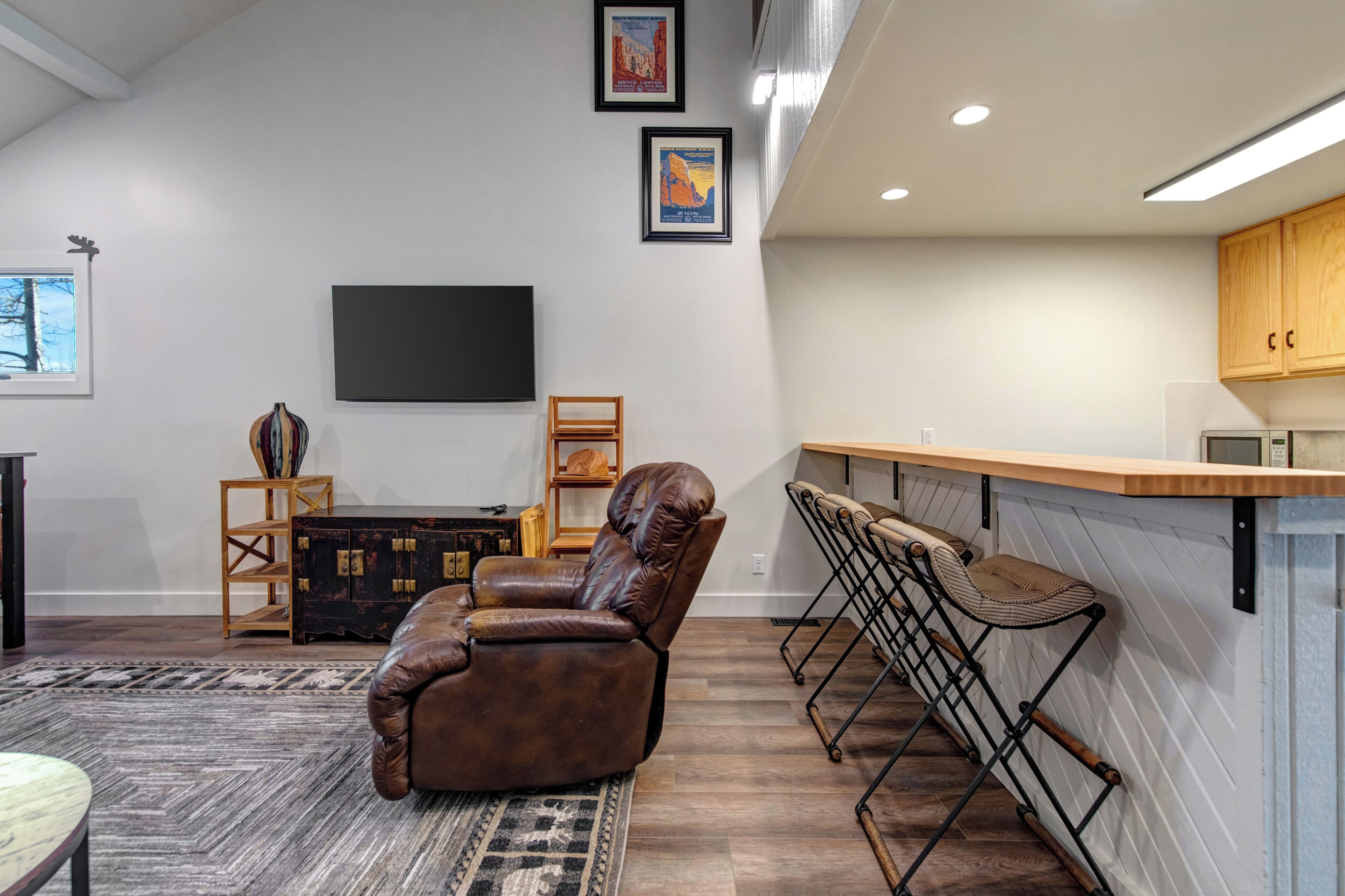 A modern living room with a leather recliner, a bar area with stools, a flat-screen TV, and a fireplace.