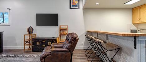 A modern living room with a leather recliner, a bar area with stools, a flat-screen TV, and a fireplace.
