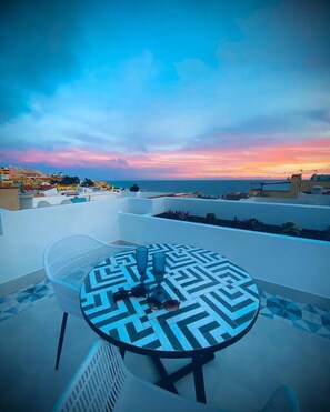 A rooftop terrace with a table and chairs, overlooking a coastal town and the sea during sunset. - AMBER Apartments `SUNNY` Studio in the city center (Morro Jable)