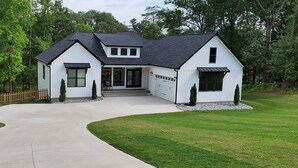Una casa a due piani con tetto scuro, rivestimento bianco e un garage.
