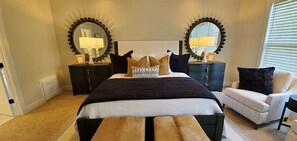 A bedroom with a bed, two nightstands with lamps, a chair, and a large mirror on the wall.