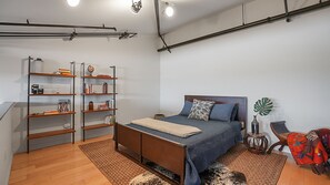 Um quarto com uma cama, uma estante de livros, uma cadeira e uma planta grande.