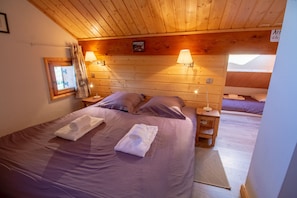 Quarto de cabana de madeira aconchegante com duas camas, cada uma com uma almofada e uma toalha dobrada. Há duas luminárias na parede, fornecendo iluminação.