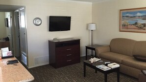Une chambre d’hôtel équipée d’une télévision à écran plat, d’un bureau avec une lampe, d’un canapé et d’un tableau au mur.