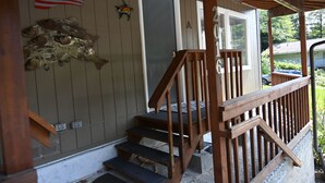A wooden porch with a staircase leading to a door, an American flag, and a turtle decoration. - Comfy Duplex Unit A great for families and small groups, sleeps up to 9 (Sitka)