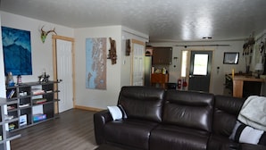A living room with a brown leather sofa, a bookshelf, and a painting on the wall. - Comfy Duplex Unit A great for families and small groups, sleeps up to 9 (Sitka)