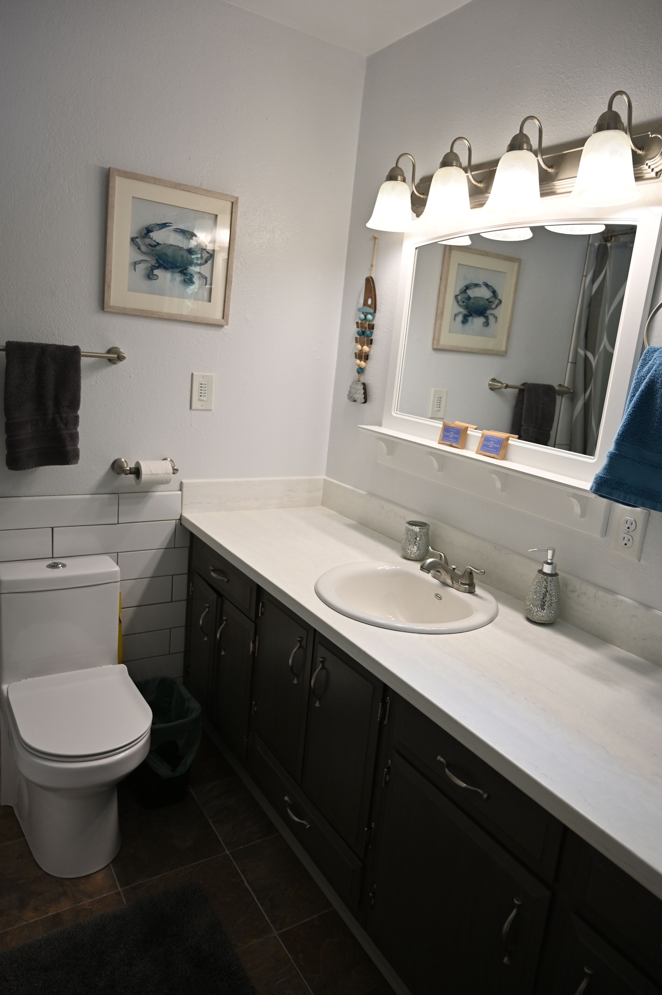 A bathroom with a white toilet, a sink with a mirror above it, and a framed picture on the wall.