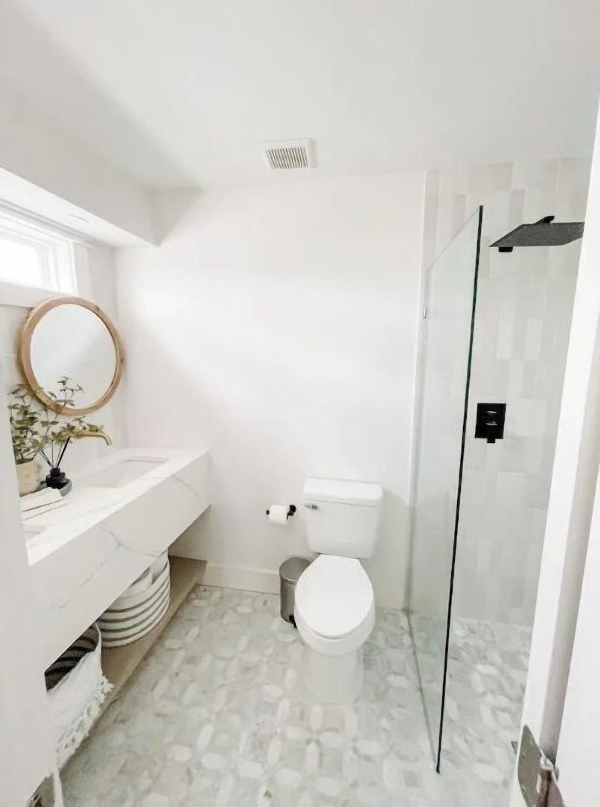 Un baño con inodoro blanco, lavabo con espejo y zona de ducha.