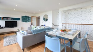 Een moderne woonkamer met een bank, televisie en eethoek met stoelen en een tafel gedekt voor een maaltijd.