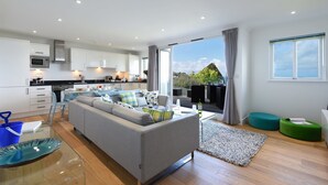 Een moderne woonruimte met een keuken, een grijze bank en uitzicht op de omgeving.