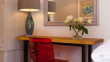 A wooden desk with a vase of white roses, a red chair, and a lamp.