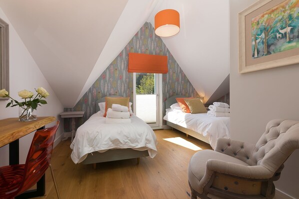 A bedroom with a sloped ceiling, a bed, a chair, and a table with a vase of flowers. - The Pearl (St Ives)