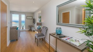 Un salón moderno con vista al mar, un sofá, una butaca, una mesa con un jarrón y un espejo grande.