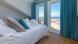 Un dormitorio con cama, almohadas y vistas a una playa a través de una ventana.