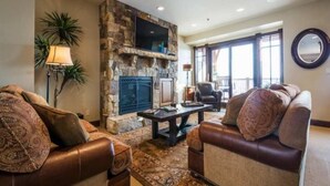 A living room with a stone fireplace, leather sofas, and a large window. - Fairway Springs by Park City Vacations (Park City)