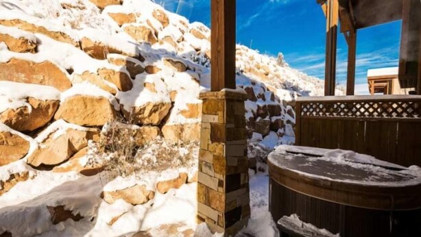 A stone building with a wooden deck and a hot tub in a snowy landscape. - Fairway Springs by Park City Vacations (Park City)