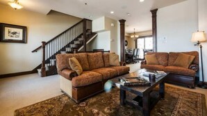 A spacious living room with a large brown sofa set, a coffee table, and a staircase leading to another level. - Fairway Springs by Park City Vacations (Park City)