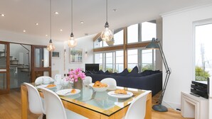 A modern dining area with a glass-top table, white chairs, and a dark-colored sofa. - Shamal (St Ives)