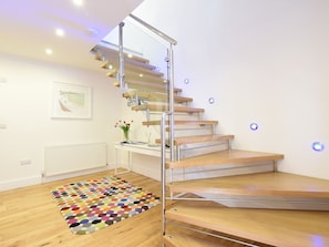 A modern staircase with glass railings and wooden steps, a colorful rug, and a small table with a vase of flowers.