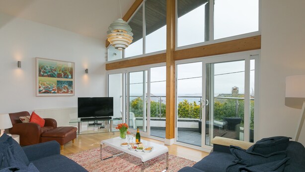 A spacious living room with a large sofa set, a flat-screen TV, and a dining area with a table set for two. - Shamal (St Ives)