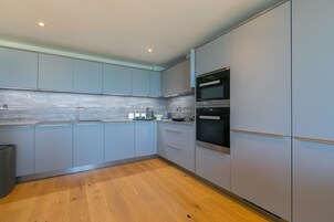Una cocina moderna con gabinetes grises, un lavamanos de acero inoxidable y dos hornos empotrados.