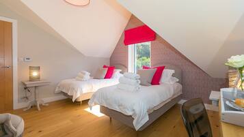 A bedroom with two beds, a small table, a chair, and a window with a red valance.