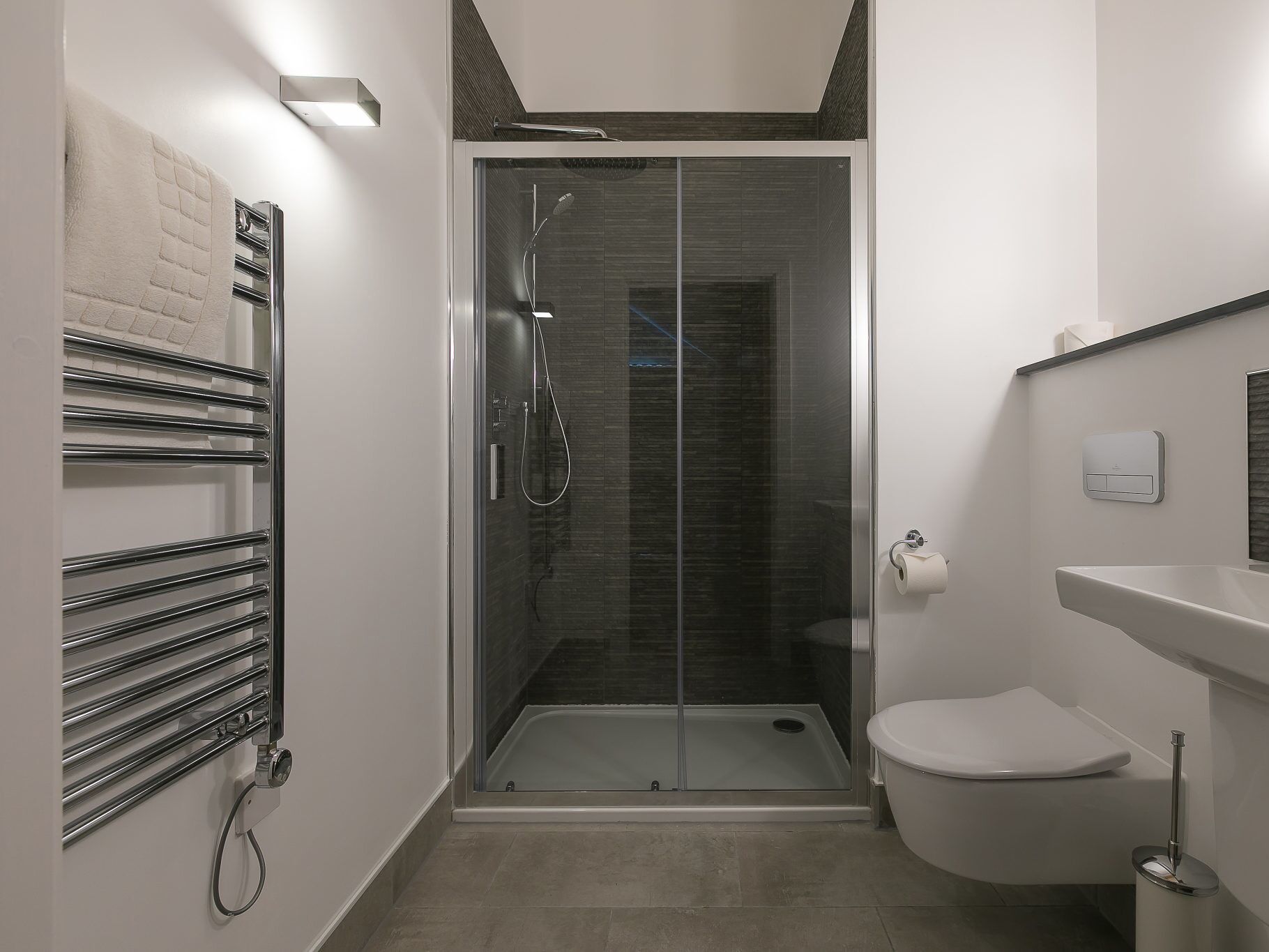 A modern bathroom with a glass-enclosed shower, a white toilet, and a towel rack.