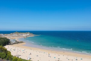 Una playa costera con vista despejada al mar, orilla de arena y edificios al fondo.