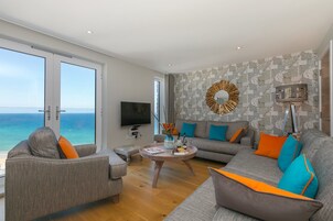 Una sala de estar moderna con un ventanal que da al mar, un televisor de pantalla plana y un espejo decorativo.