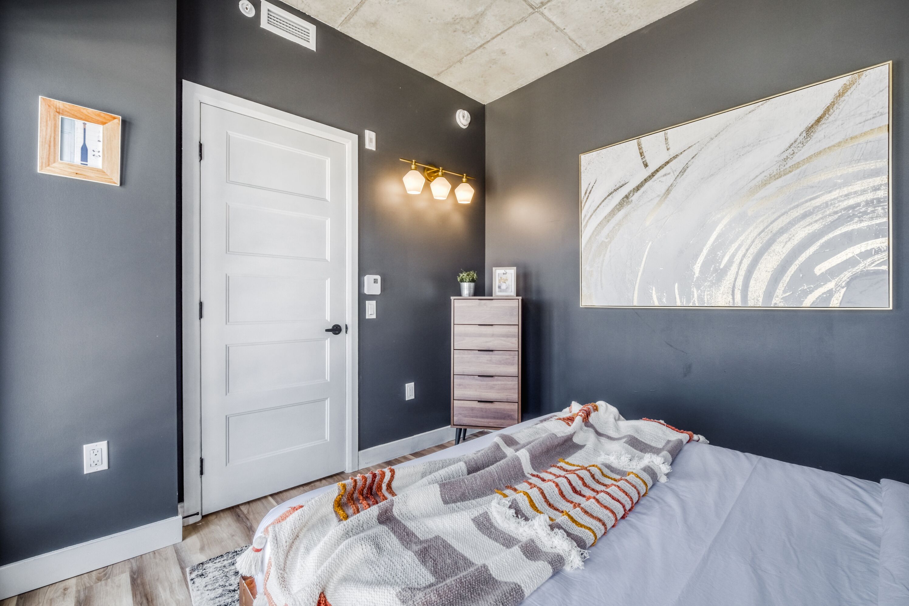 Un dormitorio con una cama, una puerta blanca, un tocador y una lámpara fijada a la pared.