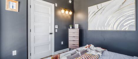 Un dormitorio con una cama, una puerta blanca, un tocador y una lámpara fijada a la pared.