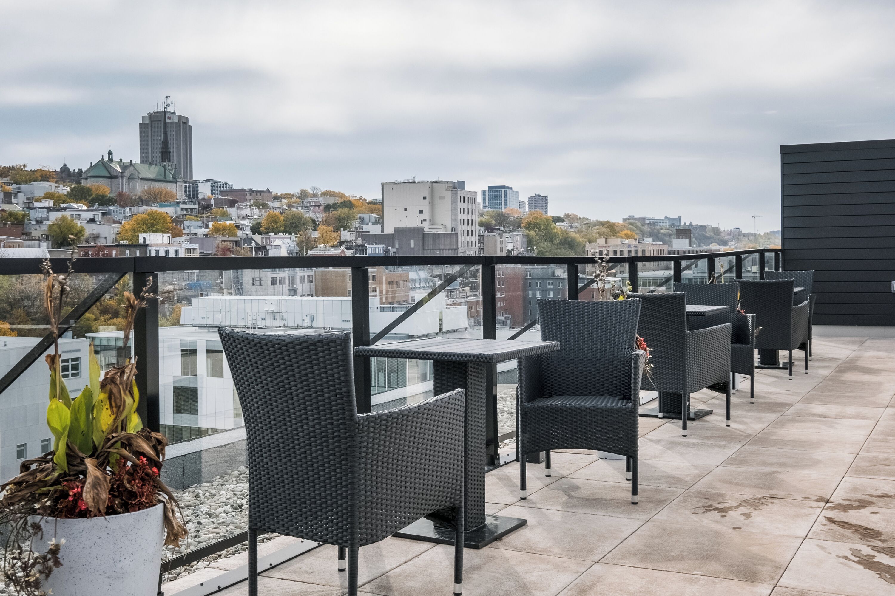 Eine Dachterrasse mit Außenbestuhlung, Blick auf die Stadtlandschaft und ein modernes Gebäude im Hintergrund.