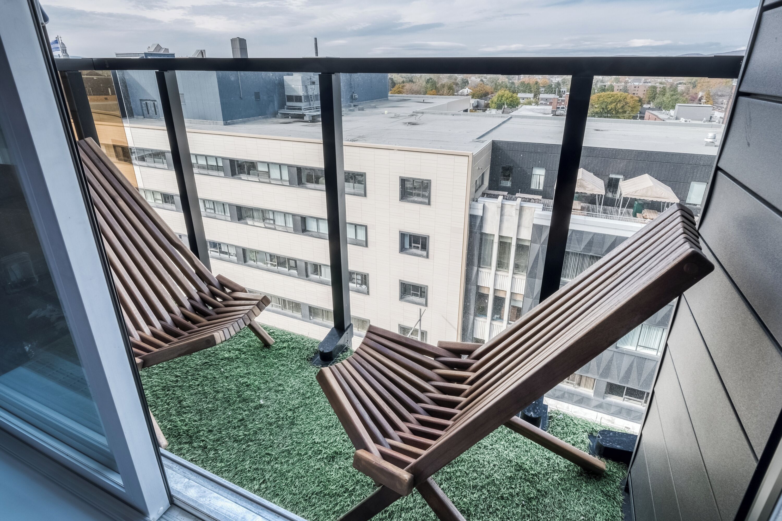 A balcony with two wooden lounge chairs and a view of a cityscape.